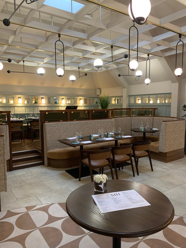 Interior of a modern restaurant featuring tables set for dining, stylish lighting fixtures, and a warm color palette.